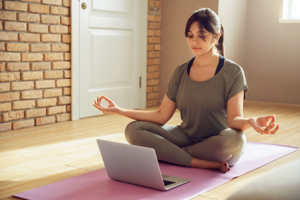 Young healthy indian woman wear sportswear meditating watching live online tv pilates class