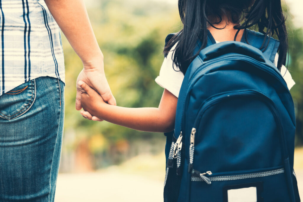 Cute asian pupil girl with backpack holding her mother hand and going to school in vintage color tone