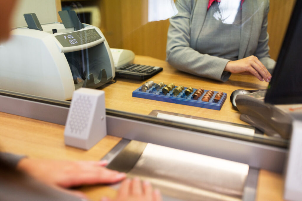 A clerk counts coins for a customer at a bank office or currency exchanger, representing the Apple Federal Credit Union overdraft fees class action.