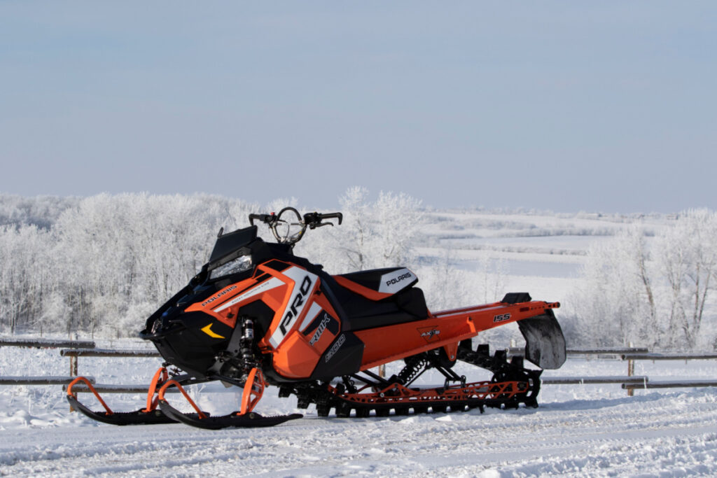 Polaris PRO800 RMK snowmobile. Sitting by a fence in a snow covered field, the long grass drenched in hoar frost.