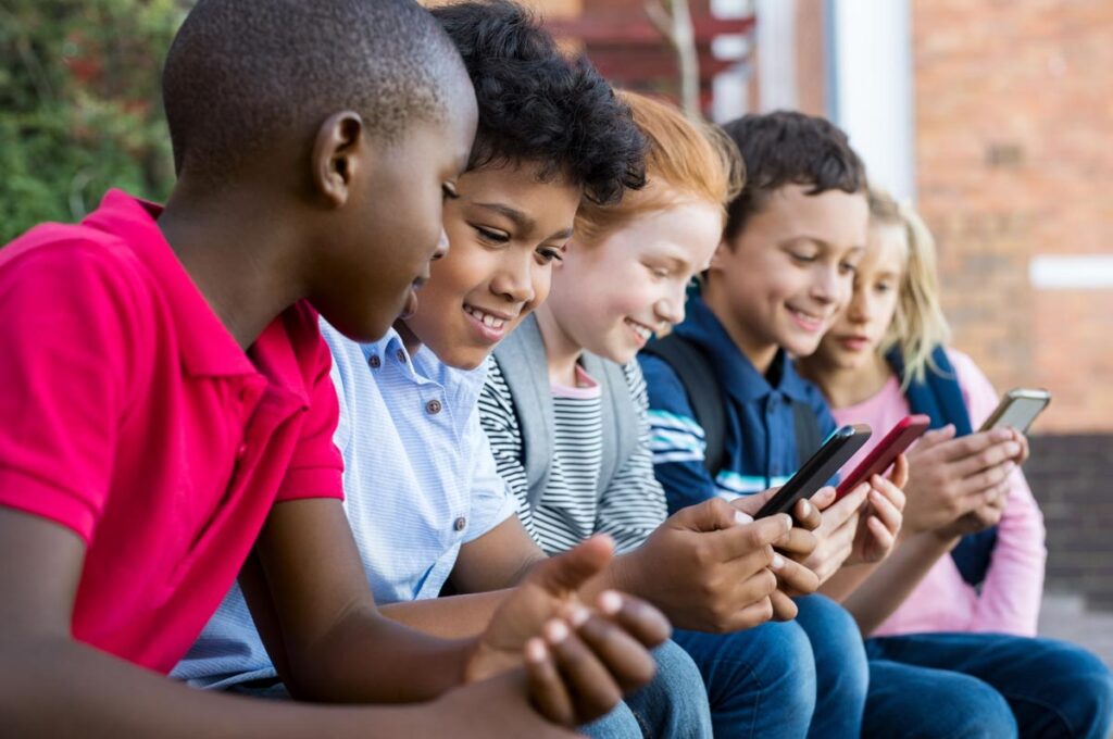 A group of young kids using their smart phone, representing social media risks.