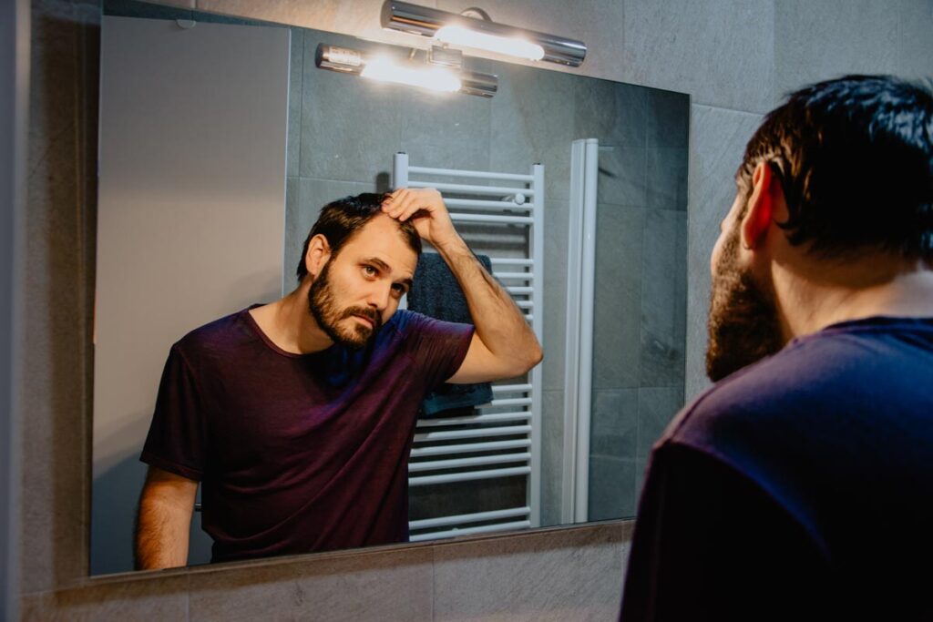 Close up of a man looking at his receding hair line in the mirror, representing the Nutrafol class action.