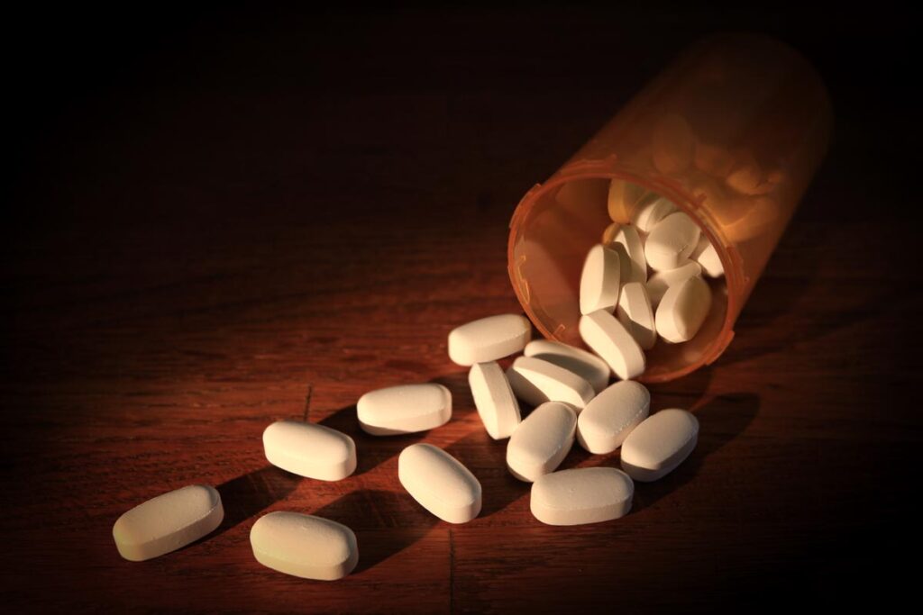 White pills scattered around a pill bottle on a tabletop, representing the Amgen-Horizon merger.