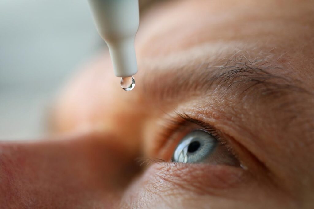 Close up of an elderly person putting eye drops in their eye, representing reports of contaminated eyedrop infections resulting in deaths.