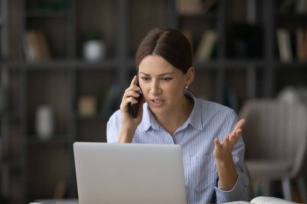 Irritated woman talking on the phone while looking at her laptop, representing the Health Insurance Associates telemarketing calls settlement.