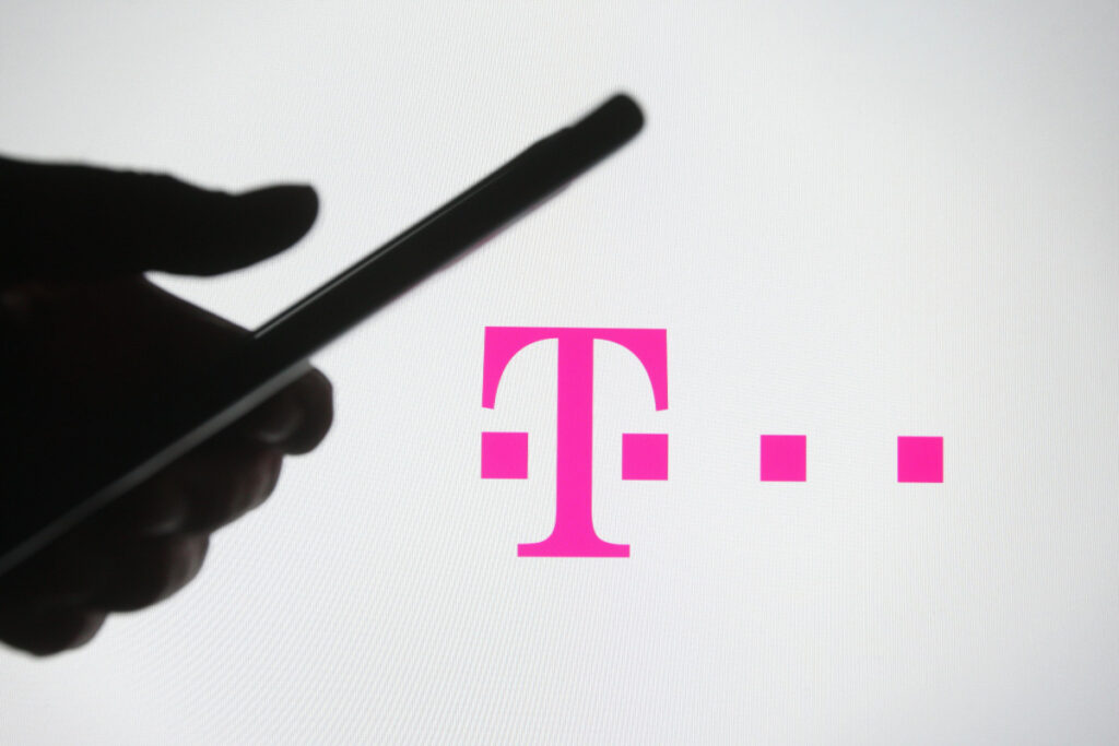 In this photo illustration a silhouette of a hand is seen holding a phone in front of T-mobile logo on a screen representing the T-Mobile data breach.
