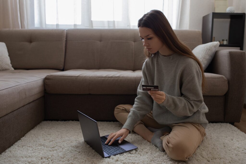 A woman sits on the floor, using her credit card and laptop to shop online, representing the Top Class Actions shopping program.