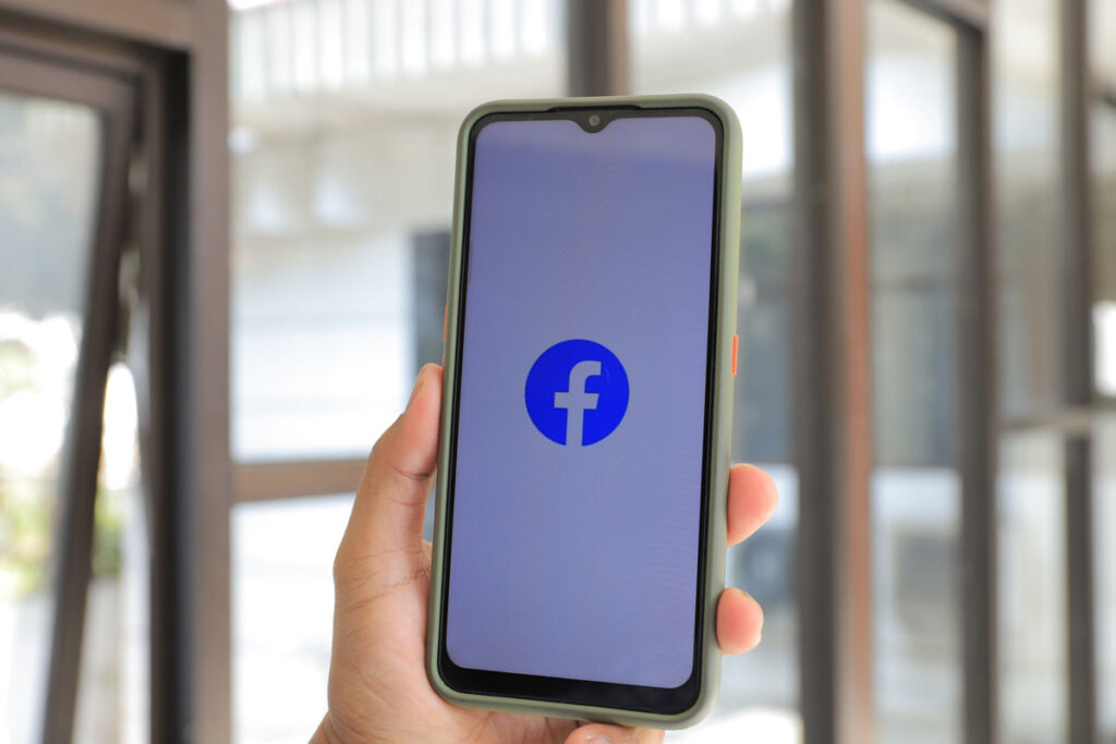 Hand holding smartphone with Facebook logo displayed on screen, representing the Facebook and Meta lawsuits and settlements.