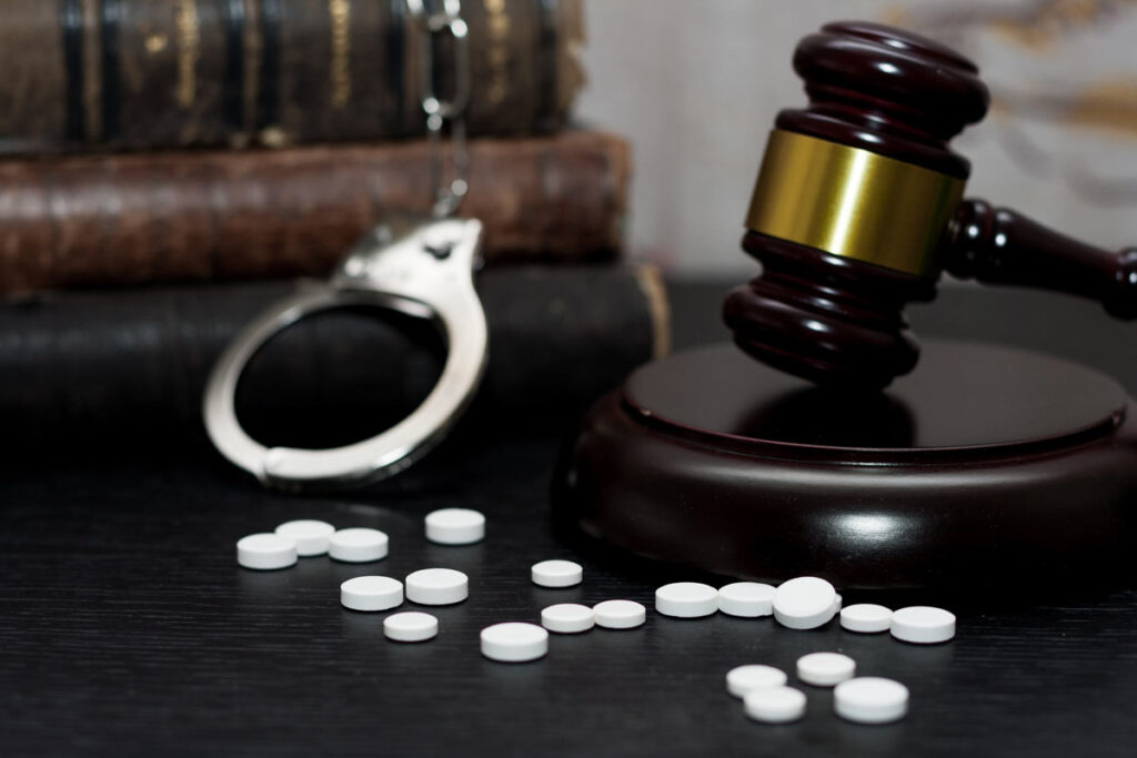 Hand cuffs, pills, and a judges gavel on a tabletop, representing a Florida man’s 15-year prison sentence for a $230 million HIV drug scheme.