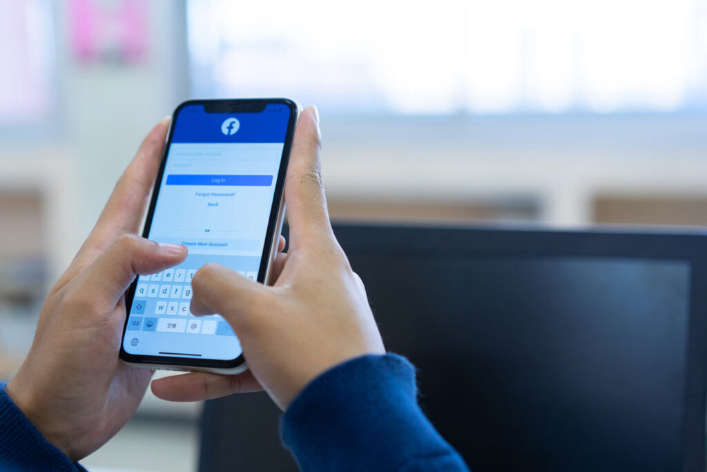 Close up of hands holding a smartphone logging into Facebook, Representing Canada’s Online News Act.