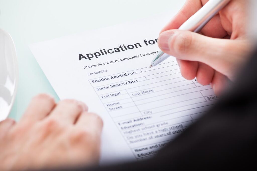 Close up of a males hands filling out a job application, representing the Kaiser Foundation Hospitals class action lawsuit settlement.