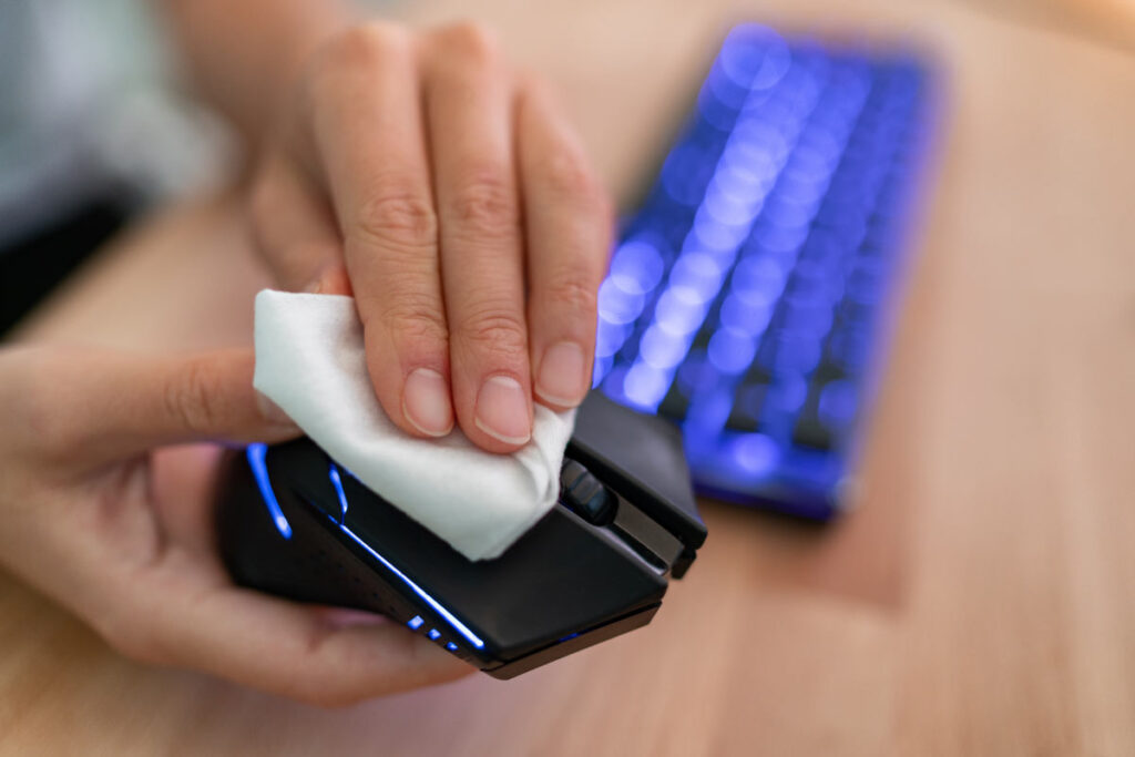 Close up of a hand cleaning a computer mouse with a wipe.