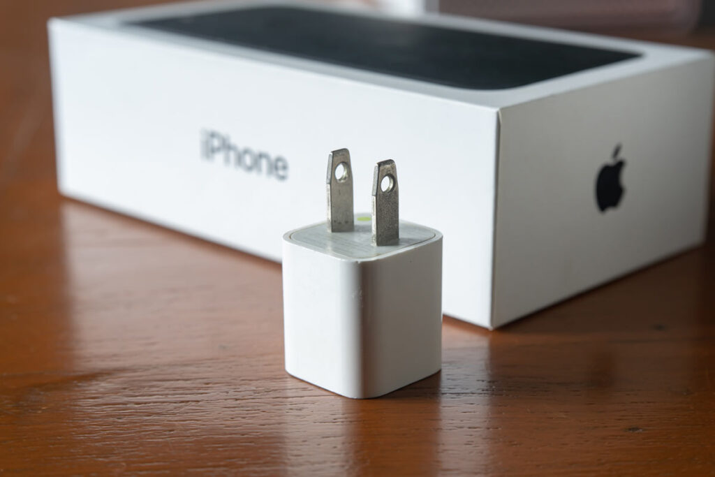 Close up of an Apple charging block, with an iPhone box in the background, representing the Apple iPhone charging block class action.