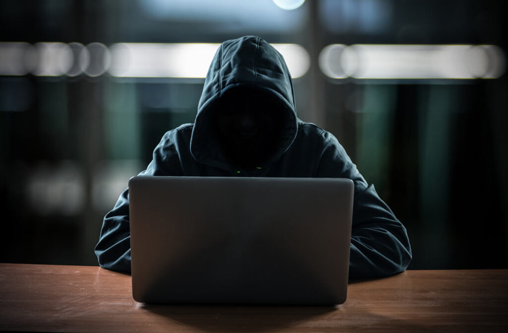 A hooded hacker behind a laptop, representing the Schneck Medical Center data breach class action settlement.