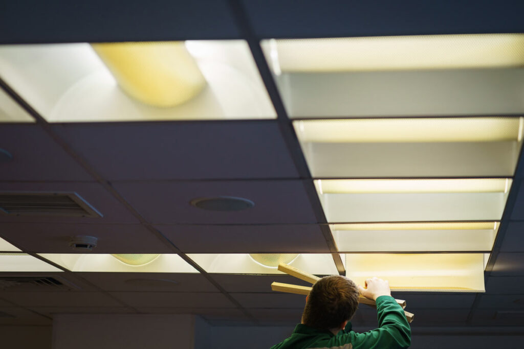 An electrician changing out ceiling lights with fluorescent bulbs, representing the Monsanto lawsuit.
