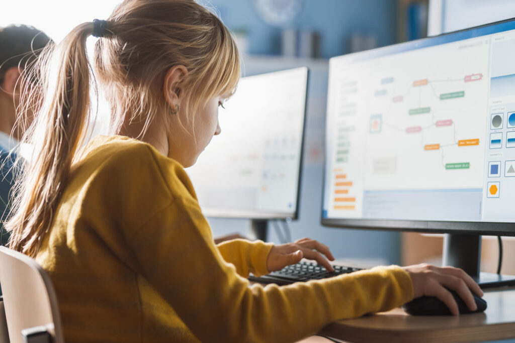 Young girl student uses a computer in a classroom, representing the FCC school cybersecurity program intended to stop cyberattacks.