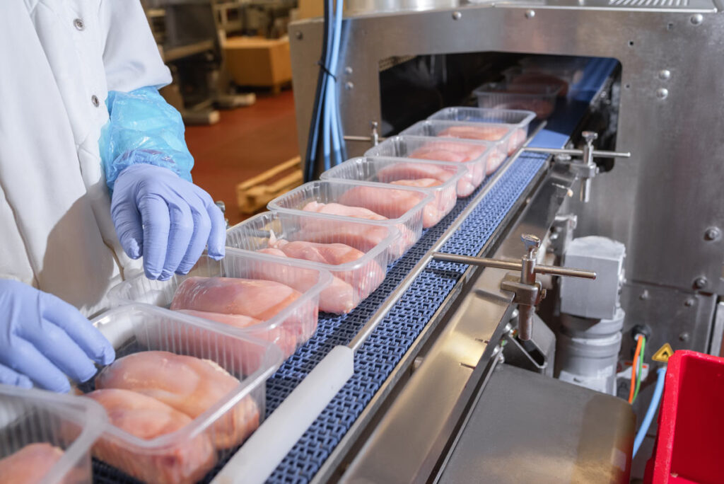 Close up of raw chicken being packaged on a conveyor belt, representing the Harrison Poultry price-fixing settlement.