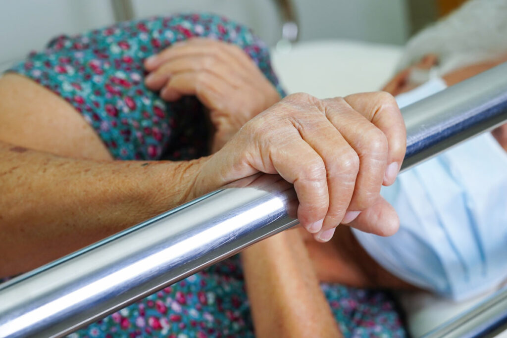 Close up of an elderly woman's hands holding a bed rail, representing adult bed rails.