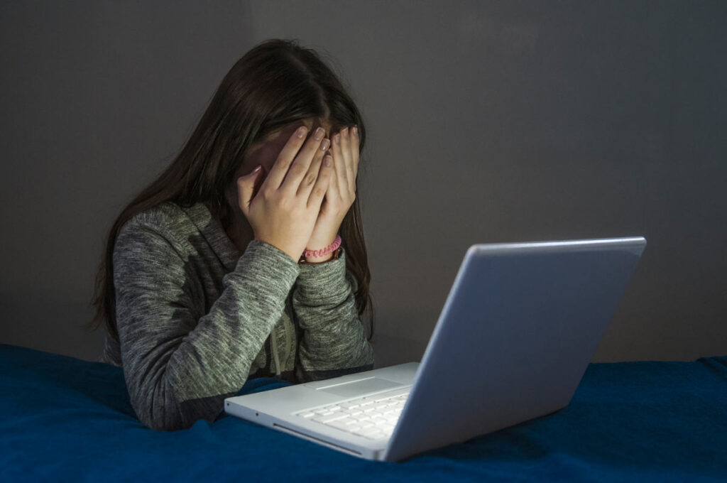 Young girl covering her face while using a laptop, cyberbullying concept, representing the Rockaway Township cyberbullying lawsuit.