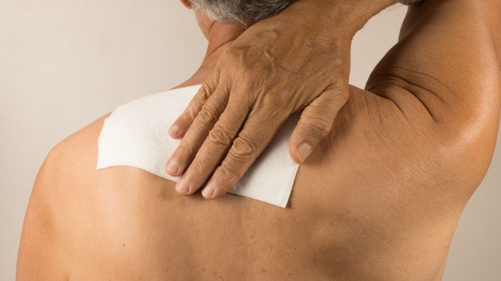 A man wearing a medicated patch for pain on his shoulder reaches behind his back to touch the patch, representing the CVS lidocaine class action lawsuit settlement.