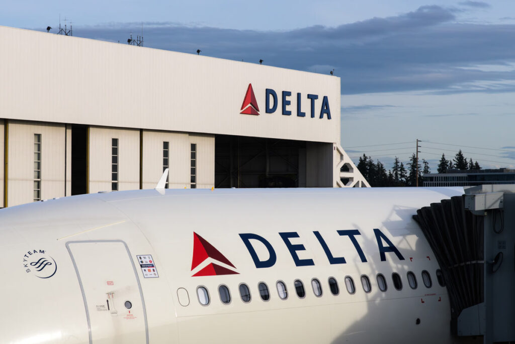 The Delta logo is seen on a hangar and plane, representing the Delta Air Lines class action lawsuit settlement.