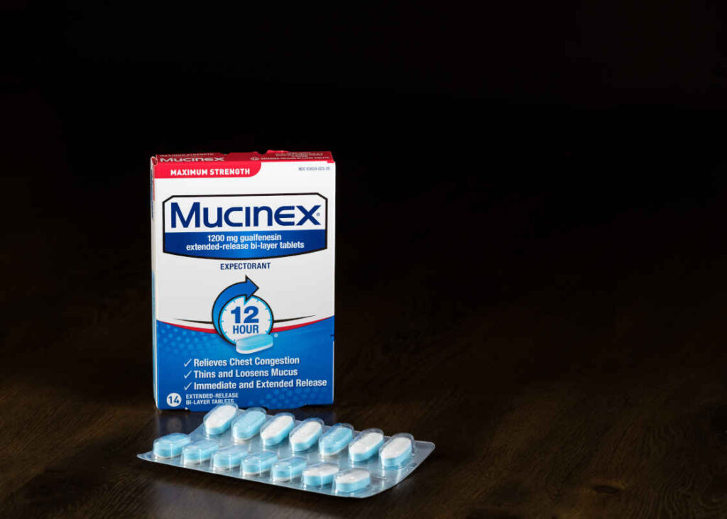 Mucinex extended release expectorant tablets and packet on wooden table representing the Mucinex and Alka Seltzer class action.