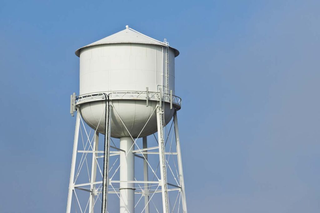 Close up of a white water tower against a blue sky, representing the PFAS water class actions.