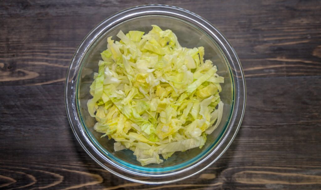 Shredded iceberg lettuce in a glass bowl on a wooden table.