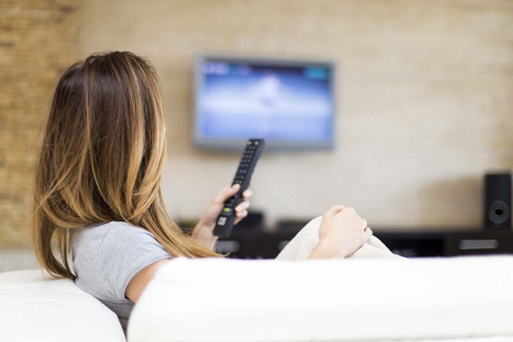 A woman watching TV in her living room, representing the tv advertising antitrust settlement.