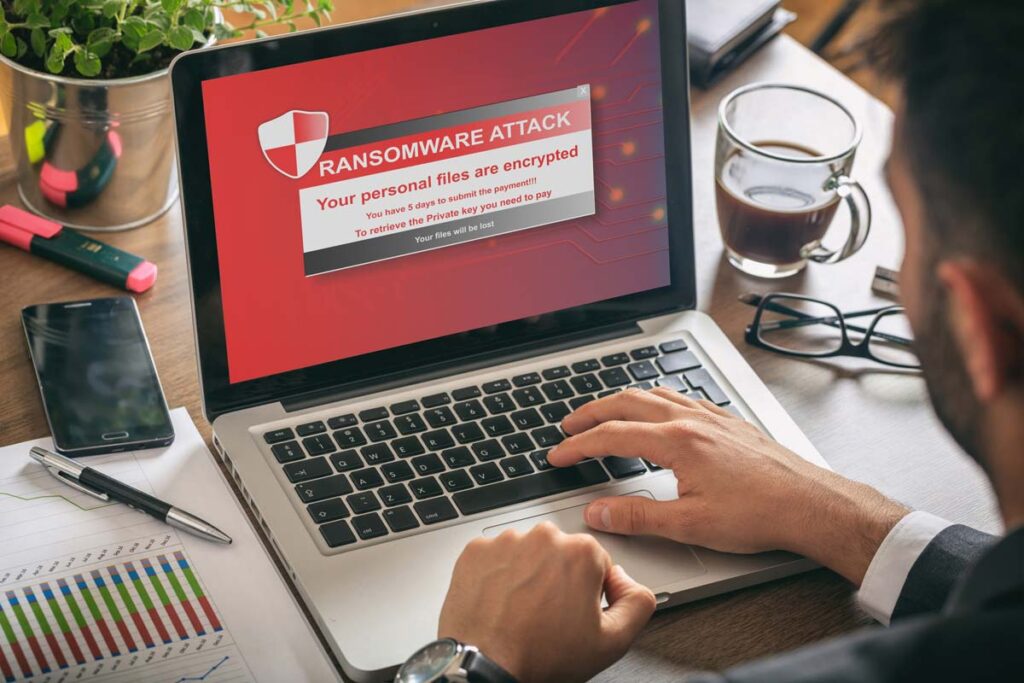 Man typing on a computer with a ransomware graphic displayed, representing the Immediate data breach settlement.