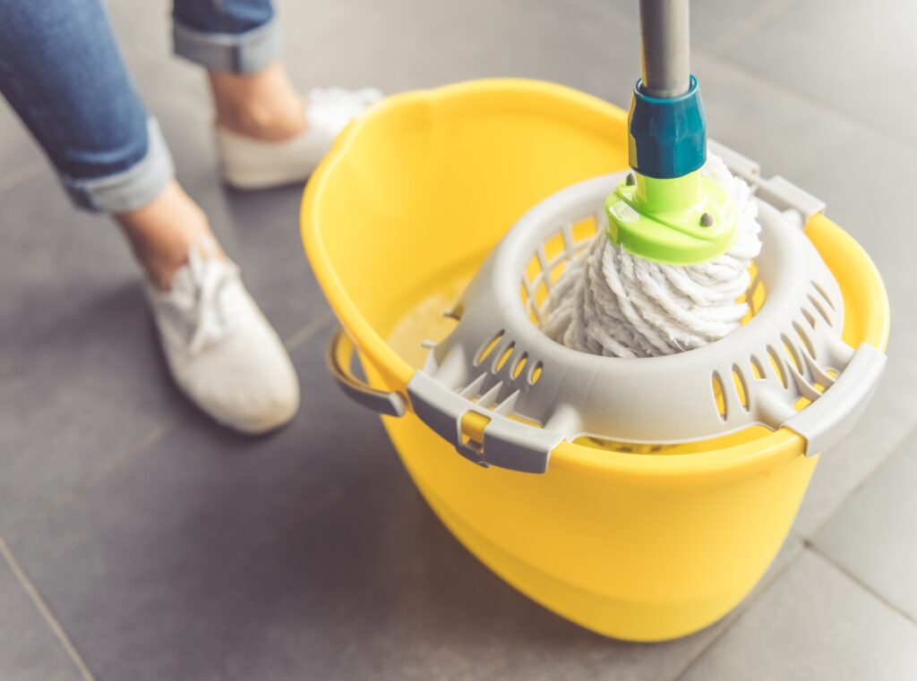 Close-up of a woman in white shoes and jeans wringing out a mop in a yellow bucket, representing the Pine-Sol settlement.