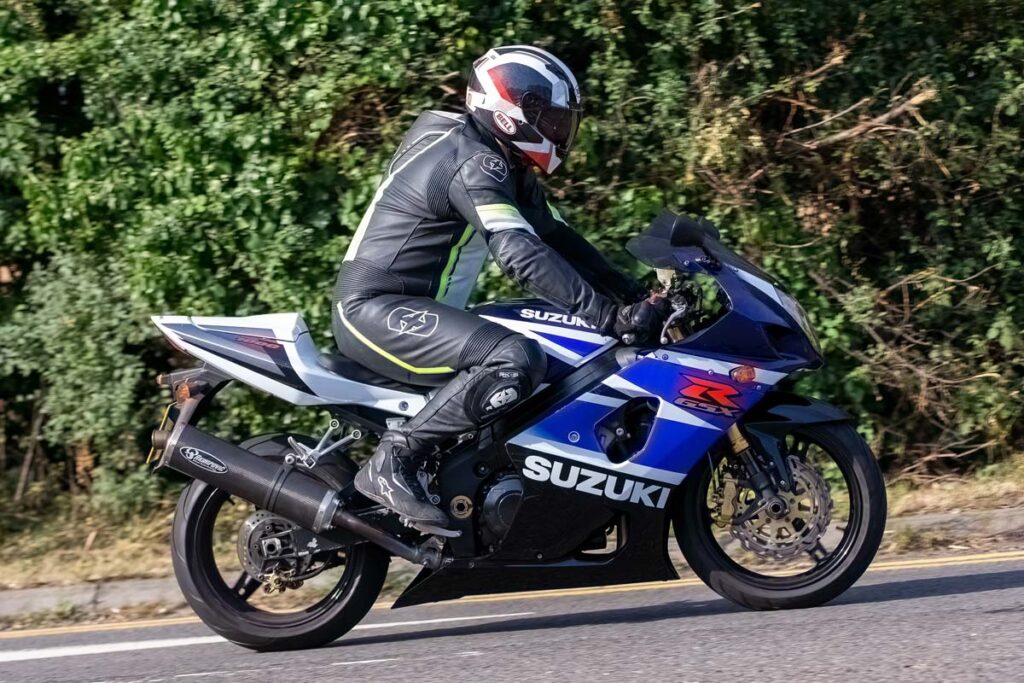 A man riding a SUZUKI GSX-R1000 motorcycle on a road, Suzuki Motor of America is facing a class action lawsuit claiming that many of its sport bikes have a defect in the front brake master cylinder (FMBC) of its sports motorcycles that can cause sudden and immediate brake failure and a safety risk for riders.