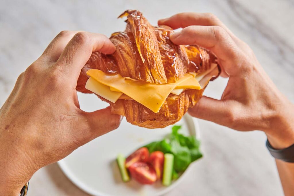 Close up of hands holding a croissant sandwich, representing the croissant sandwich recall.