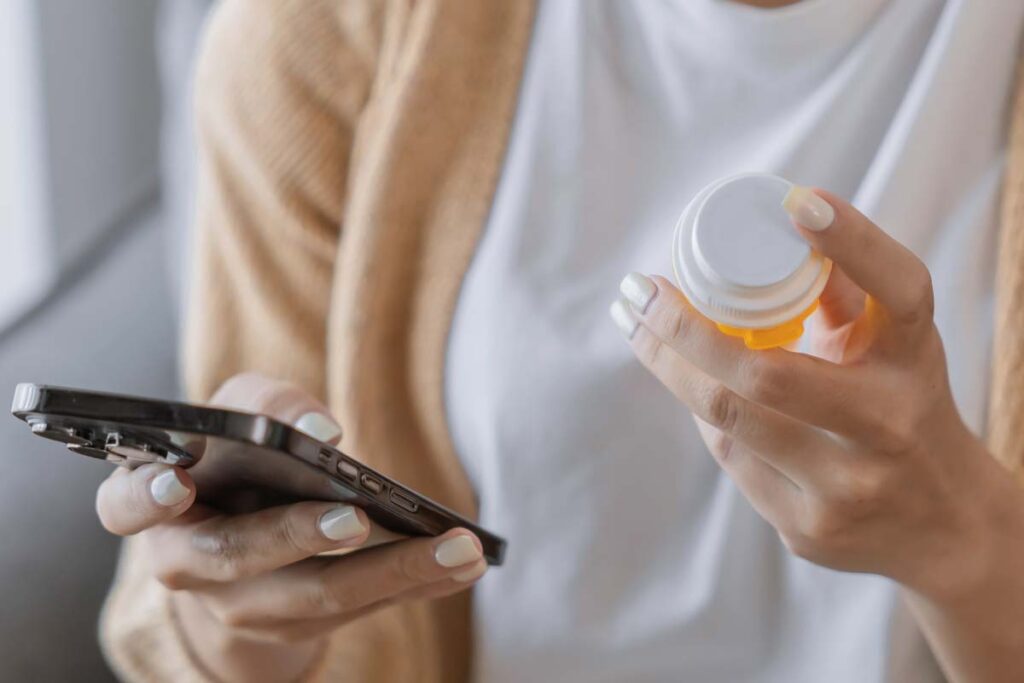 Close up of a woman holding her smartphone and a pill bottle to refill a prescription, representing the Postmeds data breach class action.