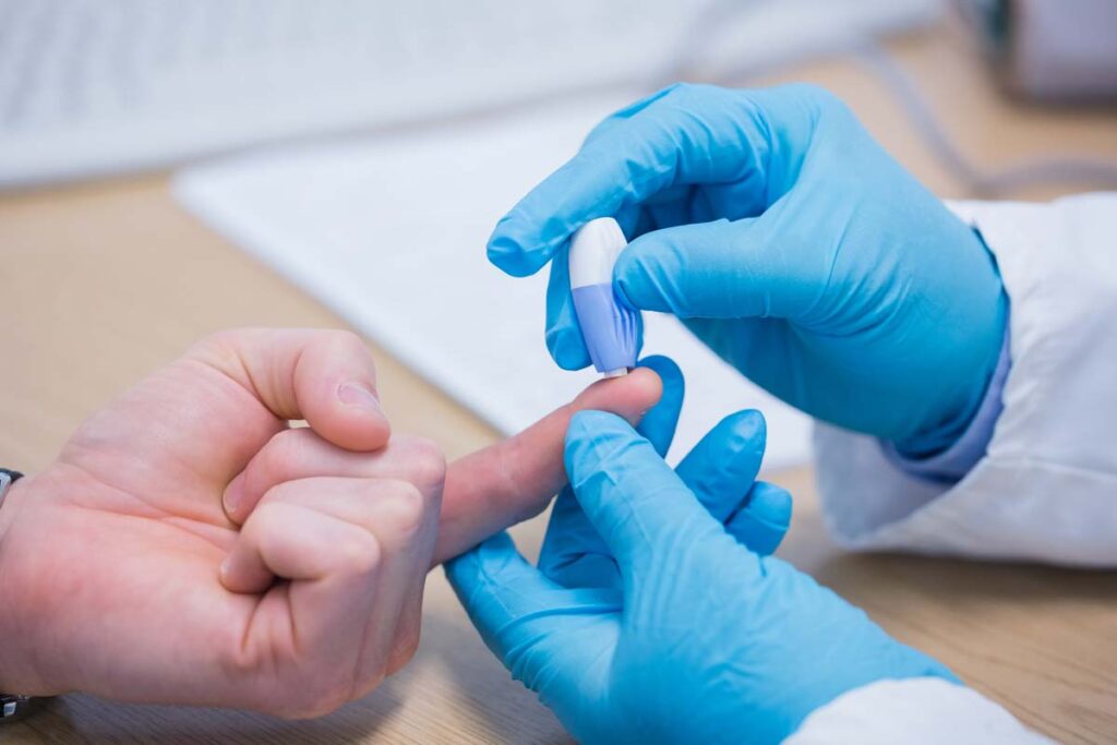 Close up of a medical professionals hands completing a finger prick blood collection, representing the Theranos class action lawsuit settlement.