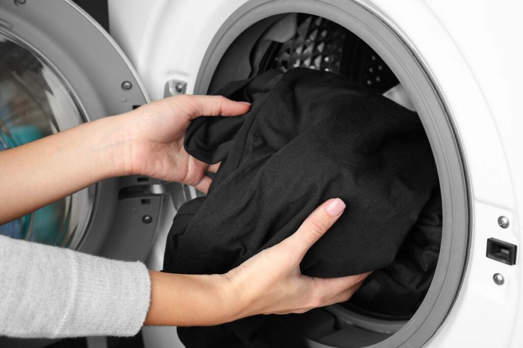 Close up of woman putting black clothes in a washer, representing the Woolite Color Renew class action lawsuit settlement.