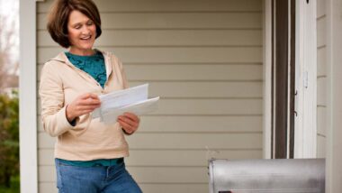 A happy woman reading mail after checking her mailbox, representing recent settlement checks in the mail.