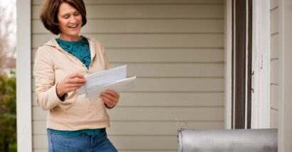 A happy woman reading mail after checking her mailbox, representing recent settlement checks in the mail.