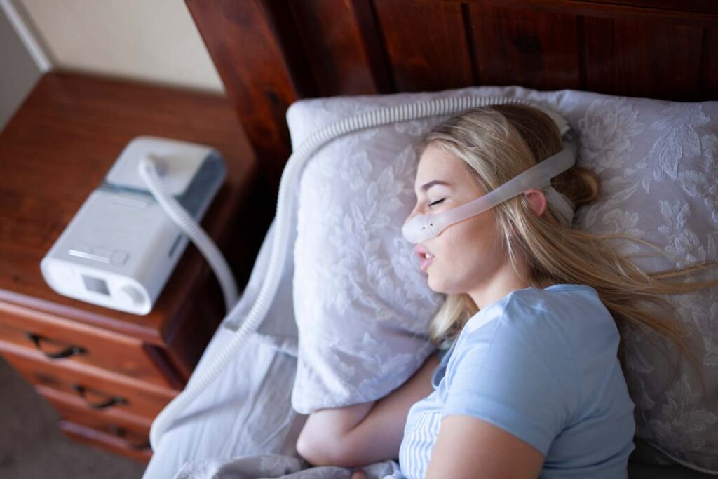 A woman using a CPAP machine while sleeping, representing the Philips CPAP class action settlement following a recall.