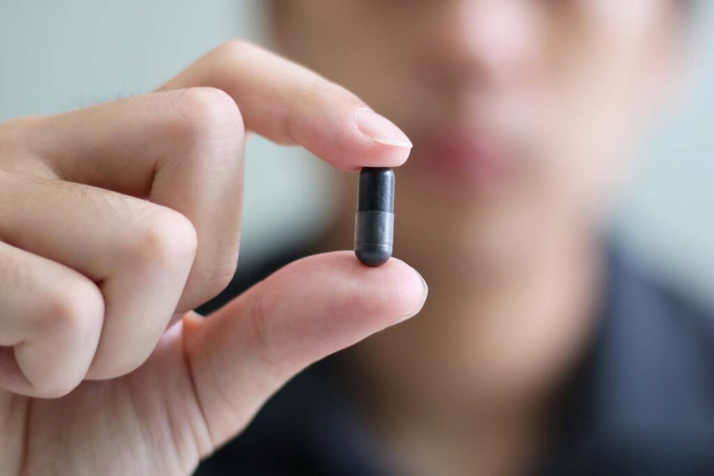 Close up of a man holding a black capsule pill, representing the Magnum XXL 9800 recall.
