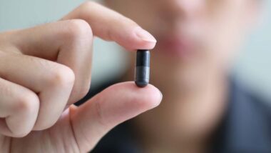 Close up of a man holding a black capsule pill, representing the Magnum XXL 9800 recall.