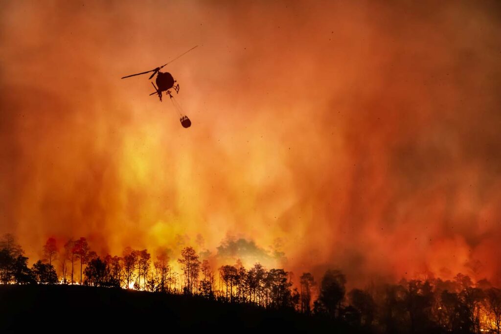 A helicopter carrying a water bucket to a large fire, representing the PacifiCorp Oregon fires settlement.