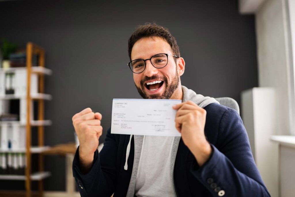 An excited man holding a check, representing recent class action settlement payouts.