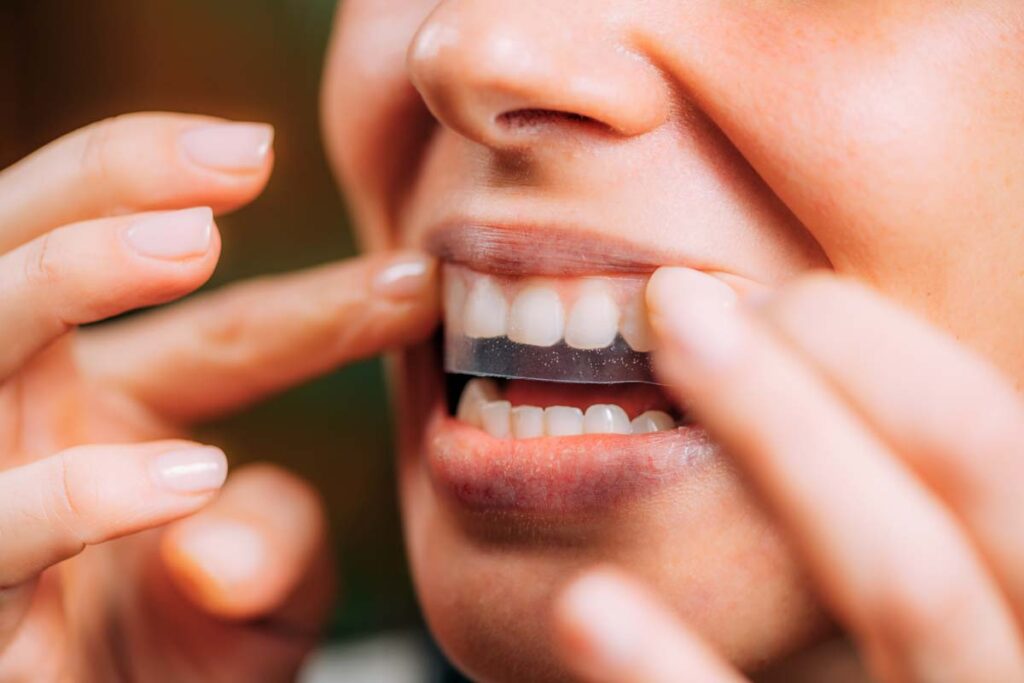 Close up of a woman putting a whitening strip on her teeth, representing the Lumineux tenth whitener class action.