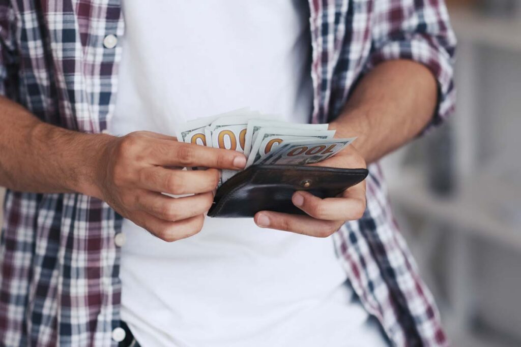 Close up of a man counting cash from his wallet, representing recent FTC refunds.