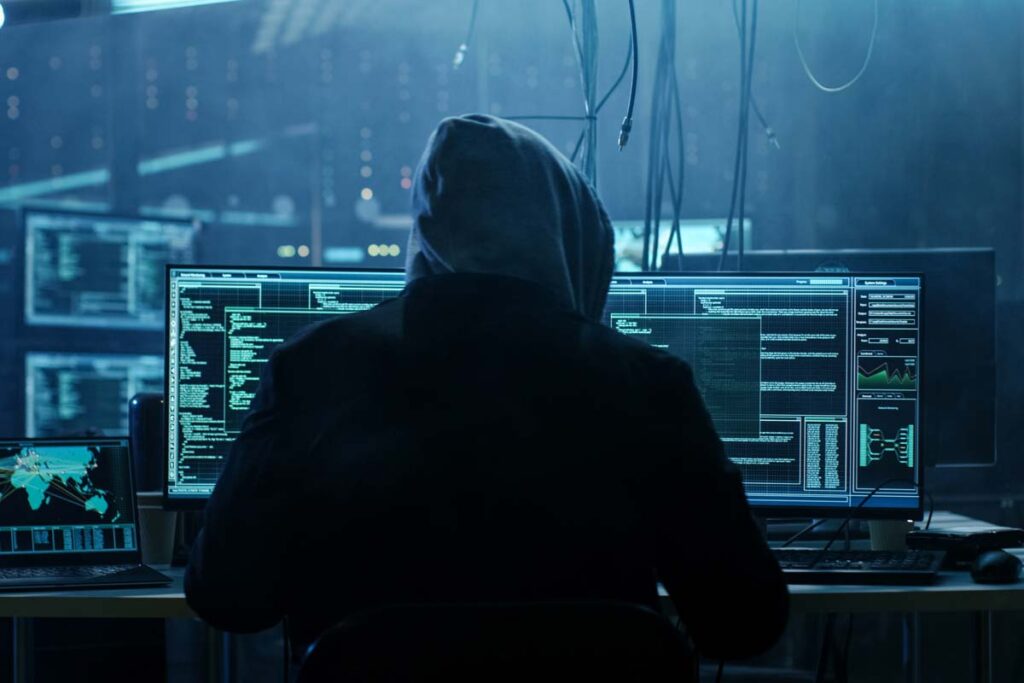 Hooded hacker using a computer, representing the AAA Collections data breach class action lawsuit settlement.