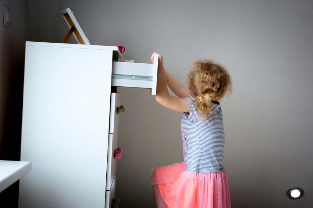 A piece of furniture tipping over as a young girl attempts to climb it, representing the furniture restraint kits.