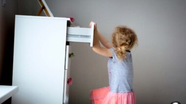 A piece of furniture tipping over as a young girl attempts to climb it, representing the furniture restraint kits.
