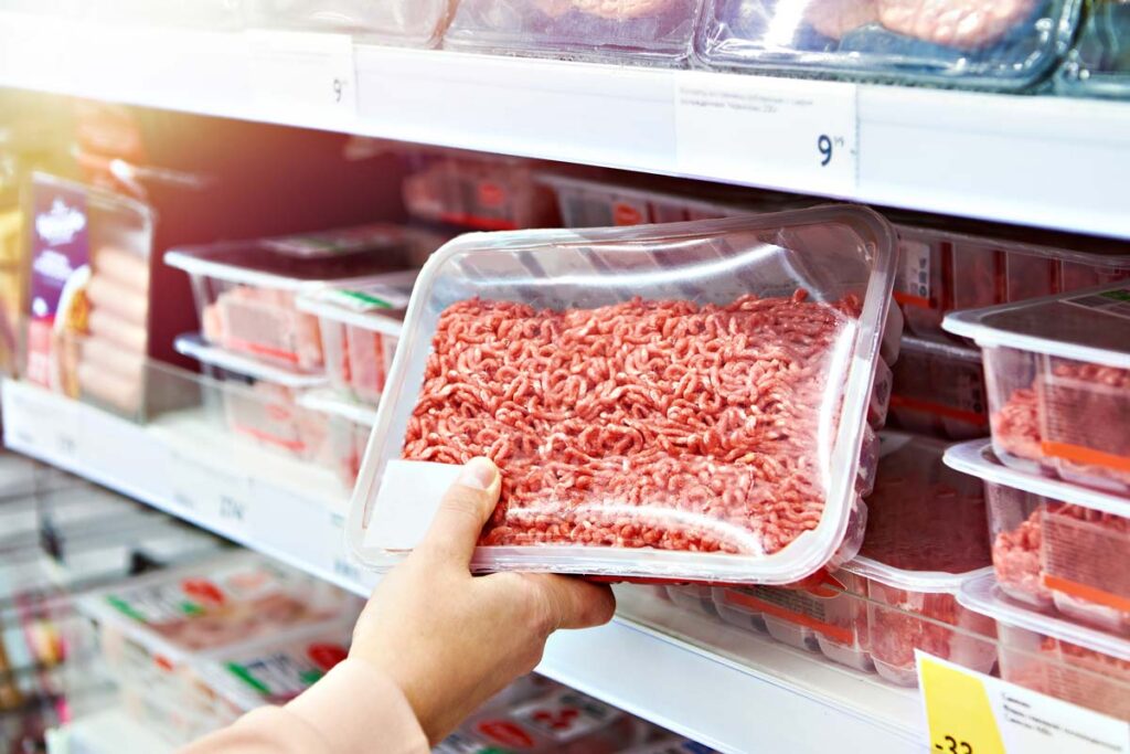 Close up of a customers hand grabbing case-ready beef from a grocery store shelf, representing the beef price-fixing direct purchasers class action settlement.