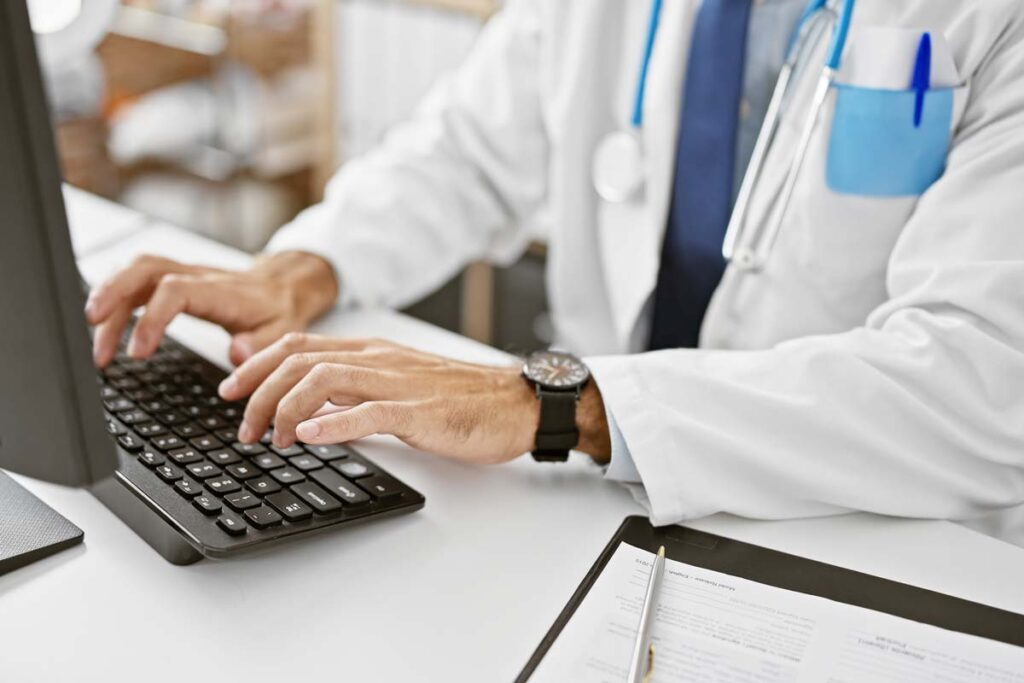 Close up of a doctor typing on a compute keyboard, representing the Norwood Clinic data breach settlement. Norwood Clinic experienced a 2022 cyber incident.